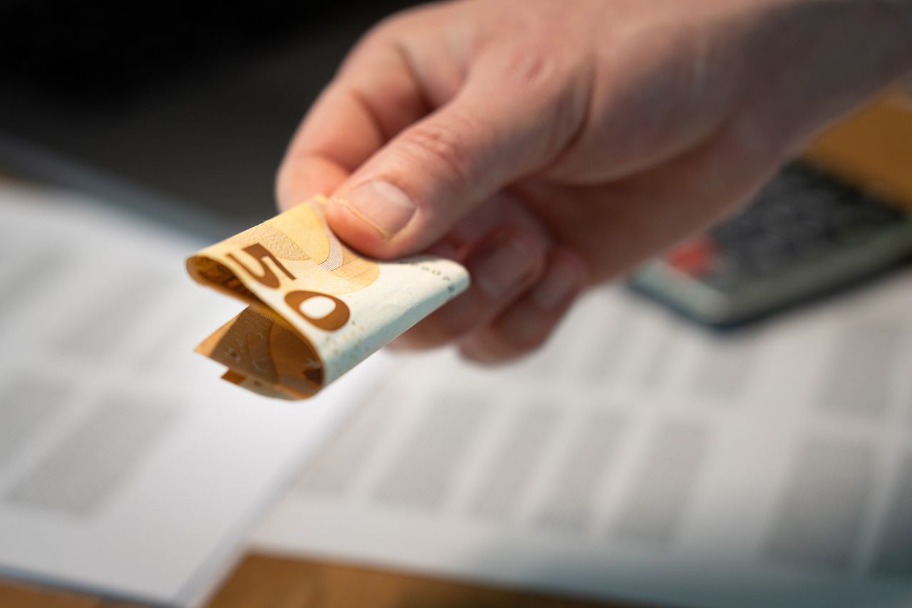 Mastering the First Impression: Your intriguing post title goes here A detailed image of a hand holding a folded 50 euro banknote, with documents in the background.